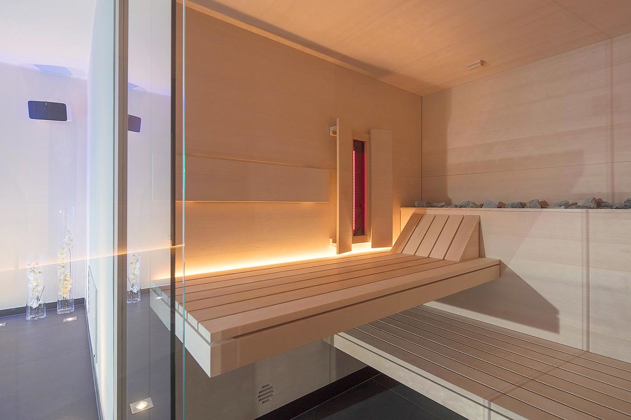Premium Sauna in Hemlockholz mit integriertem Infrarotstrahler und Hinterbankofen. Moderne Glasfront. Maßanfertigung direkt vom Saunahersteller.