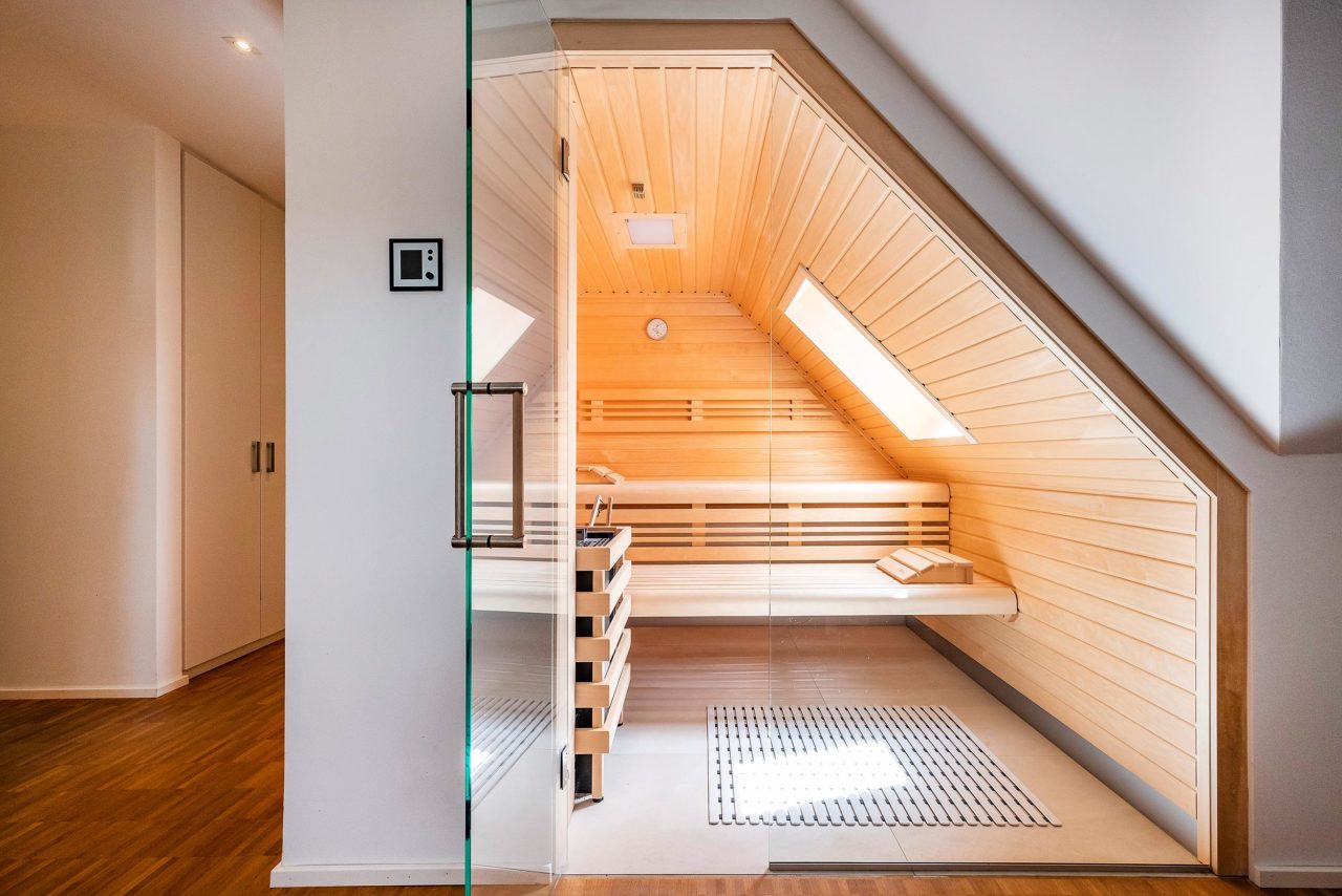 Helle Sauna unter Dachschräge mit integriertem Veluxfenster und Glasfront. Moderne, helle Heimsauna für Zuhause.